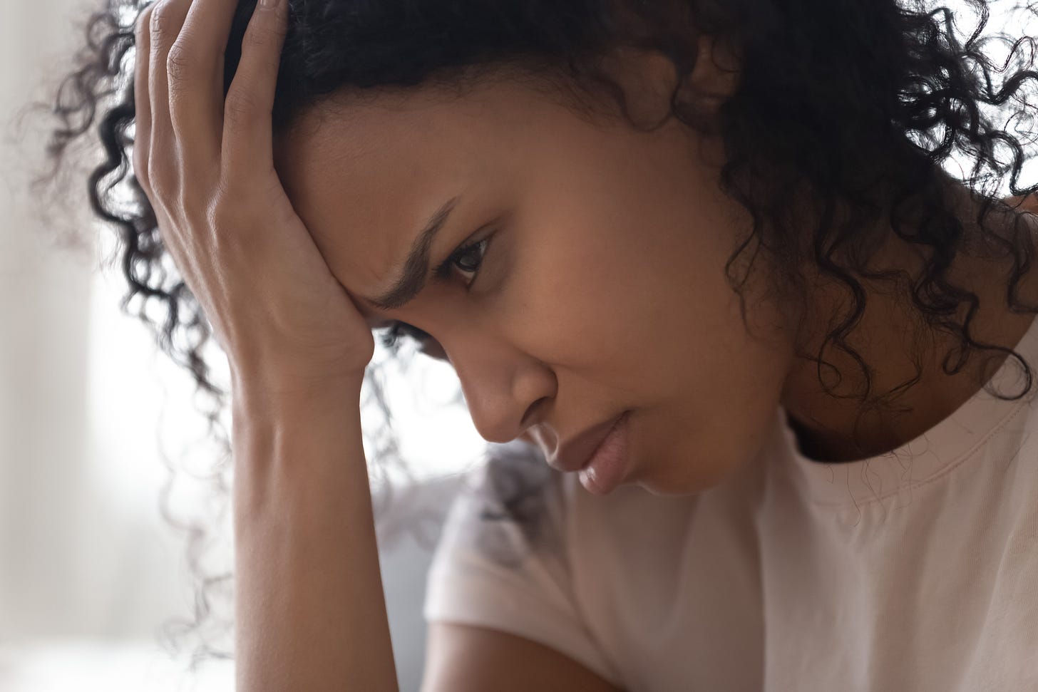 Photo of young black woman with her head in her hands, looking unhappy