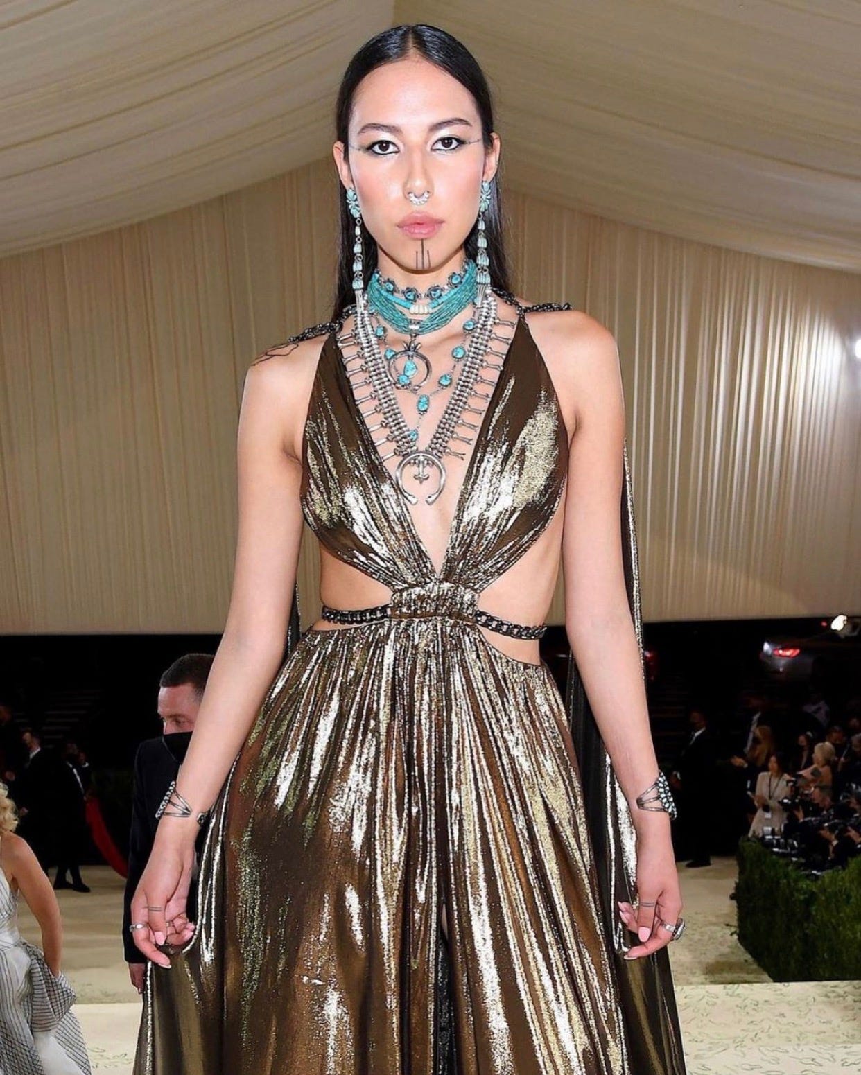 Indigenous model & activist Quannah Chasinghorse in a custom #DUNDASXREVOLVE gold lamé gown at the 2021 Met Gala. She completed her look with traditional Navajo jewelry (turquoise & silver earrings and necklaces) gifted to her by her aunt.