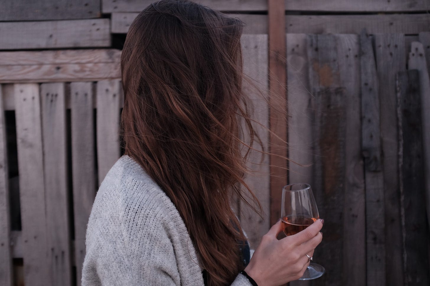 Side profile of a white woman holding a glass of wine, with her long brown hair obscuring her face.