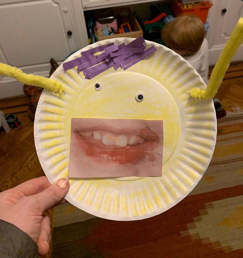 A horrific paper plate and pipecleaner art creation featuring the demogorgon-like teeth of a small child cut out from a photograph and two small beady googly eyes