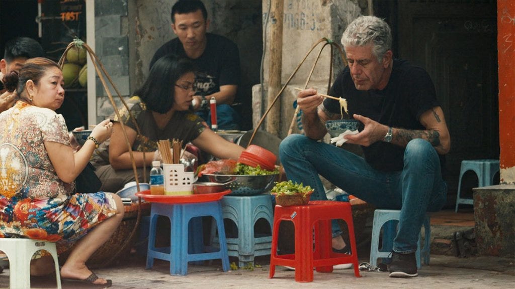 A still from Roadrunner. Anthony Bourdain sits on a stool eating a bowl of noodles.