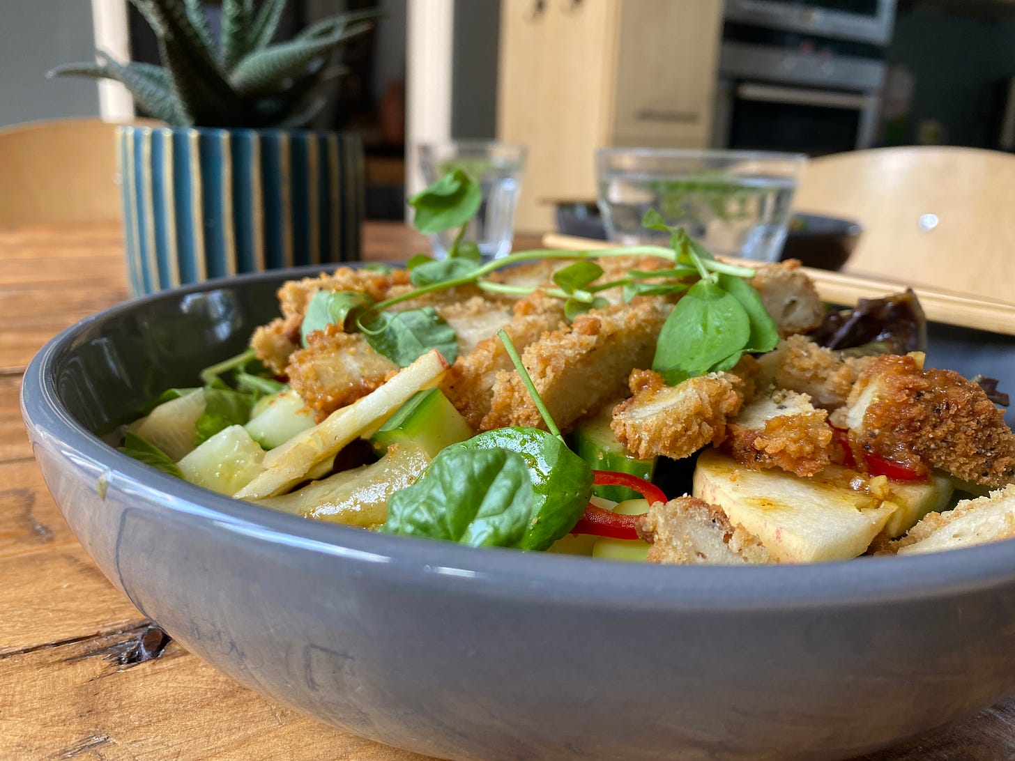 Bowl of salad with breaded chicken and pieces of spinach, apple and chilli