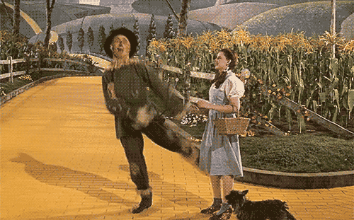 Scarecrow dancing on the Yellow brick road as Dorothy and Toto look on. From the film The Wizard of Oz