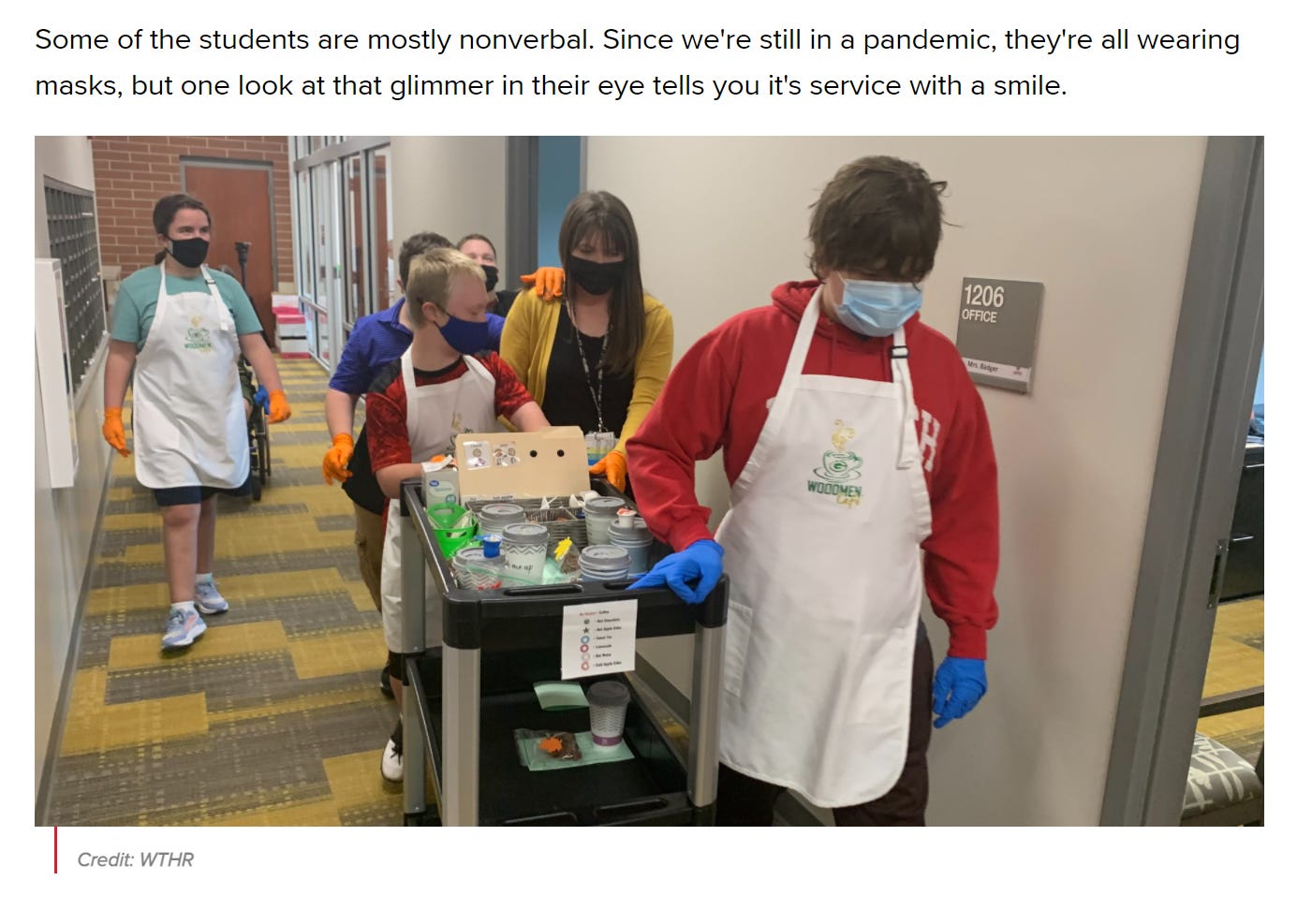 [image] students walking down an office hallway with a cart of coffee and treats for school staff, students are wearing aprons with a Woodmen cafe logo as well as facemasks; text reads: Some of the students are mostly nonverbal. Since we’re still in a pandemic, they’re all wearing masks, but one look at that glimmer in their eye tells you it’s service with a smile