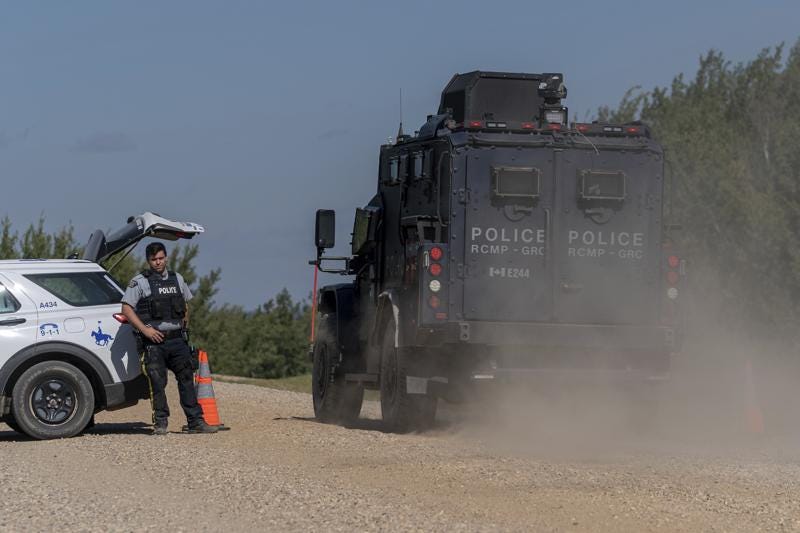 An armored RCMP vehicle, right, drives past a police roadblock set up on the James Smith Cree First Nation reservation in Saskatchewan, Canada, Tuesday, Sept. 6, 2022, as they search for a suspect in a series of stabbings. (Heywood Yu/The Canadian Press via AP)