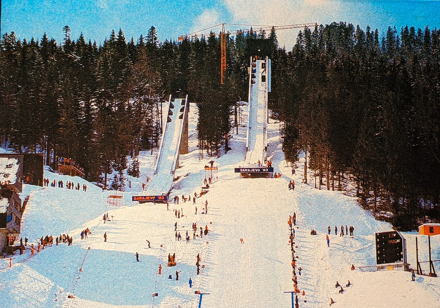 A picture of the ski jumps covered in snow, people in orange snow suits gathered around the bottom. 