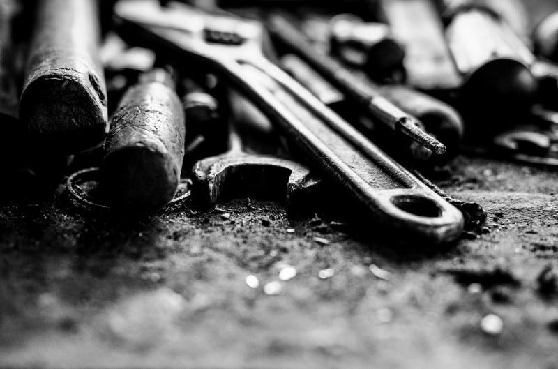 tools on a workbench, mostly wrenches, a crescent wrench closest to hand.