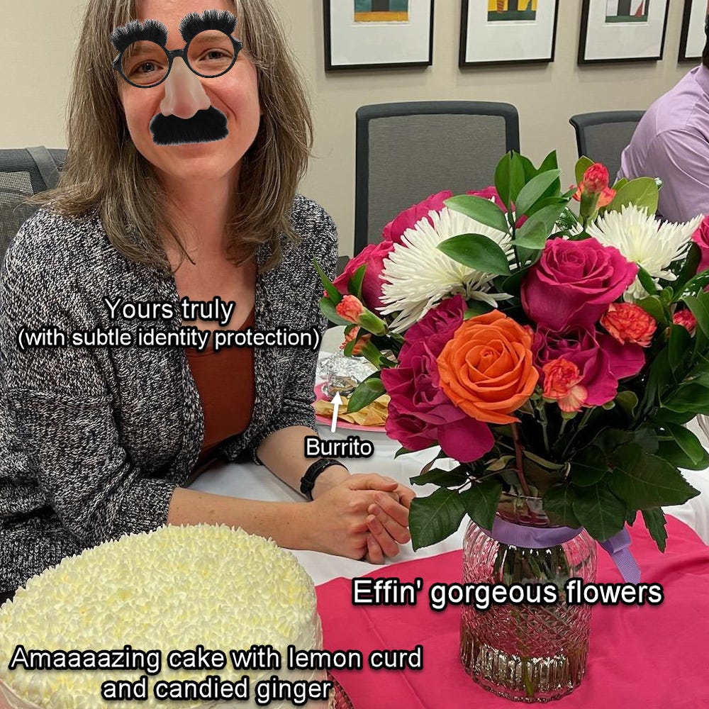 Photo of the author with photoshopped Groucho glasses sitting at a conference table next to an iced lemon-ginger cake and a bouquet of orange and magenta roses; a foil-wrapped burrito lurks at the author's elbow