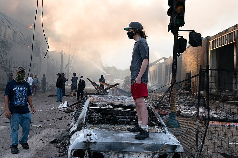 File:A man stands on a burned out car on Thursday morning as fires burn behind him in the Lake St area of Minneapolis, Minnesota (49945886467).jpg