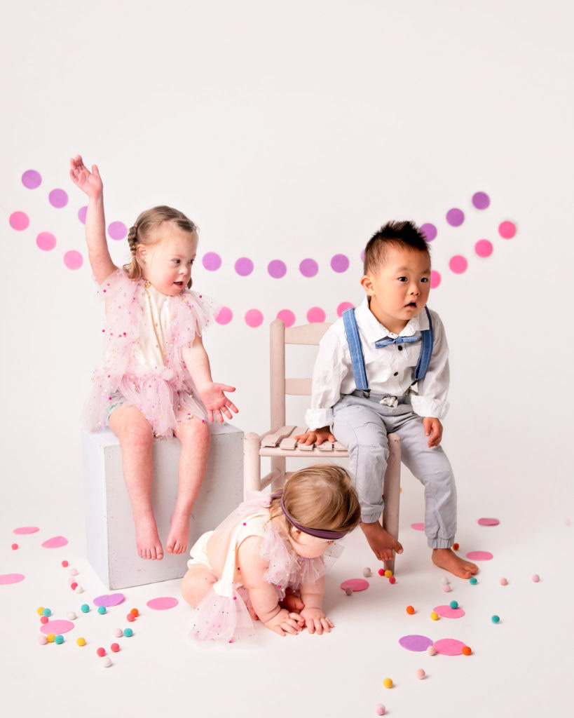 Three special needs children infront of white studio background, with colorful decorations