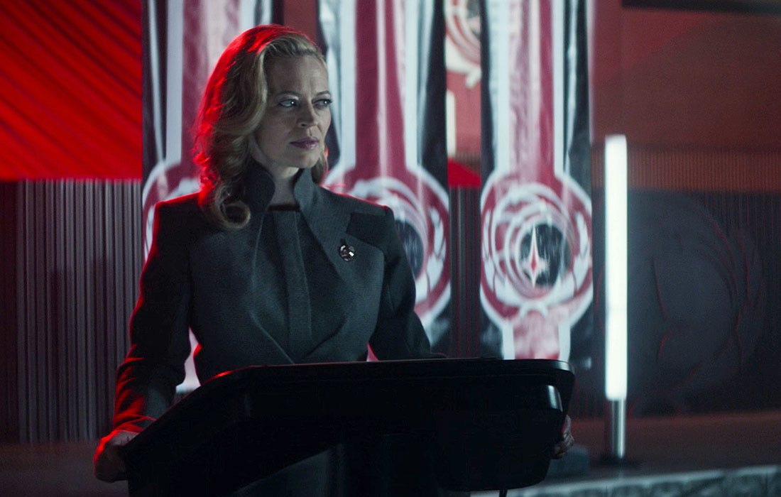 This image shows Seven of Nine (played by Jeri Ryan) as Confederation President Annika Hansen standing at a lectern about to deliver her annual Eradication Day address. Seven/Hansen stands in front of several Confederation flags. This image shows Seven of Nine (played by Jeri Ryan) as Confederation President Annika Hansen standing at a lectern about to deliver her annual Eradication Day address. Seven/Hansen stands in front of several Confederation flags.