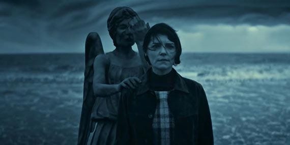 This image shows Claire Brown (played by Annabel Scholey) standing in front of the rogue Weeping Angel that possesses her mind in Doctor Who: Flux's fourth chapter / episode (titled "Village of the Angels"). The Angel touches Claire's shoulder with its right hand while holding its left hand over its face. They stand on a beach in front of rolling ocean surf. This image shows Claire Brown (played by Annabel Scholey) standing in front of the rogue Weeping Angel that possesses her mind in Doctor Who: Flux's fourth chapter / episode (titled "Village of the Angels"). The Angel touches Claire's shoulder with its right hand while holding its left hand over its face. They stand on a beach in front of rolling ocean surf.