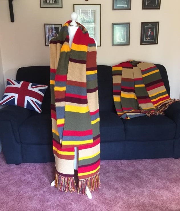 A full body headless mannequin wearing an 18 foot stripy Dr Who scarf with an identical scarf draped on a black couch in the background.