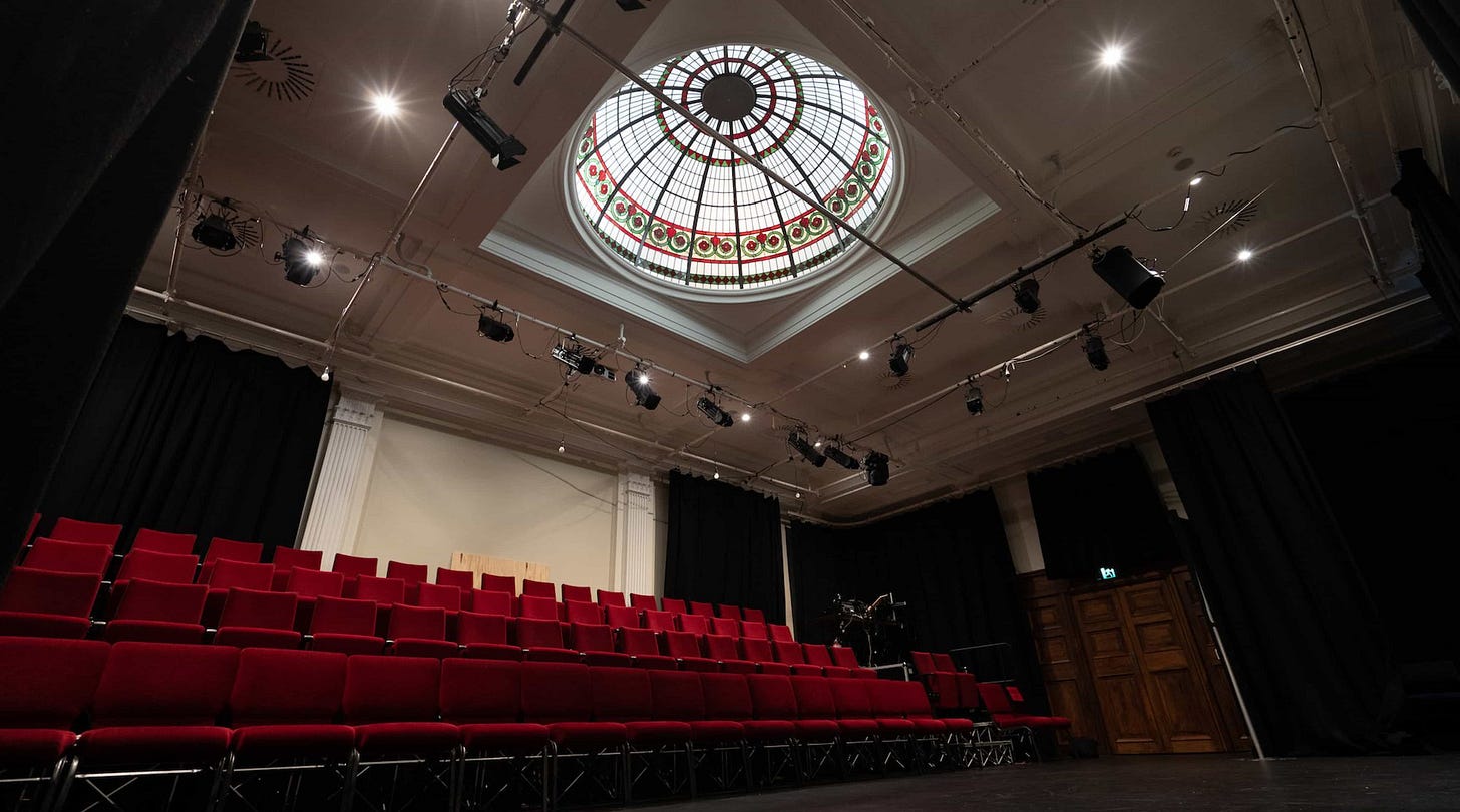 A picture of inside the Dome theatre at BATS. It shows the red seating block and the roof with lights, including the glass dome lit as if it is daytime.