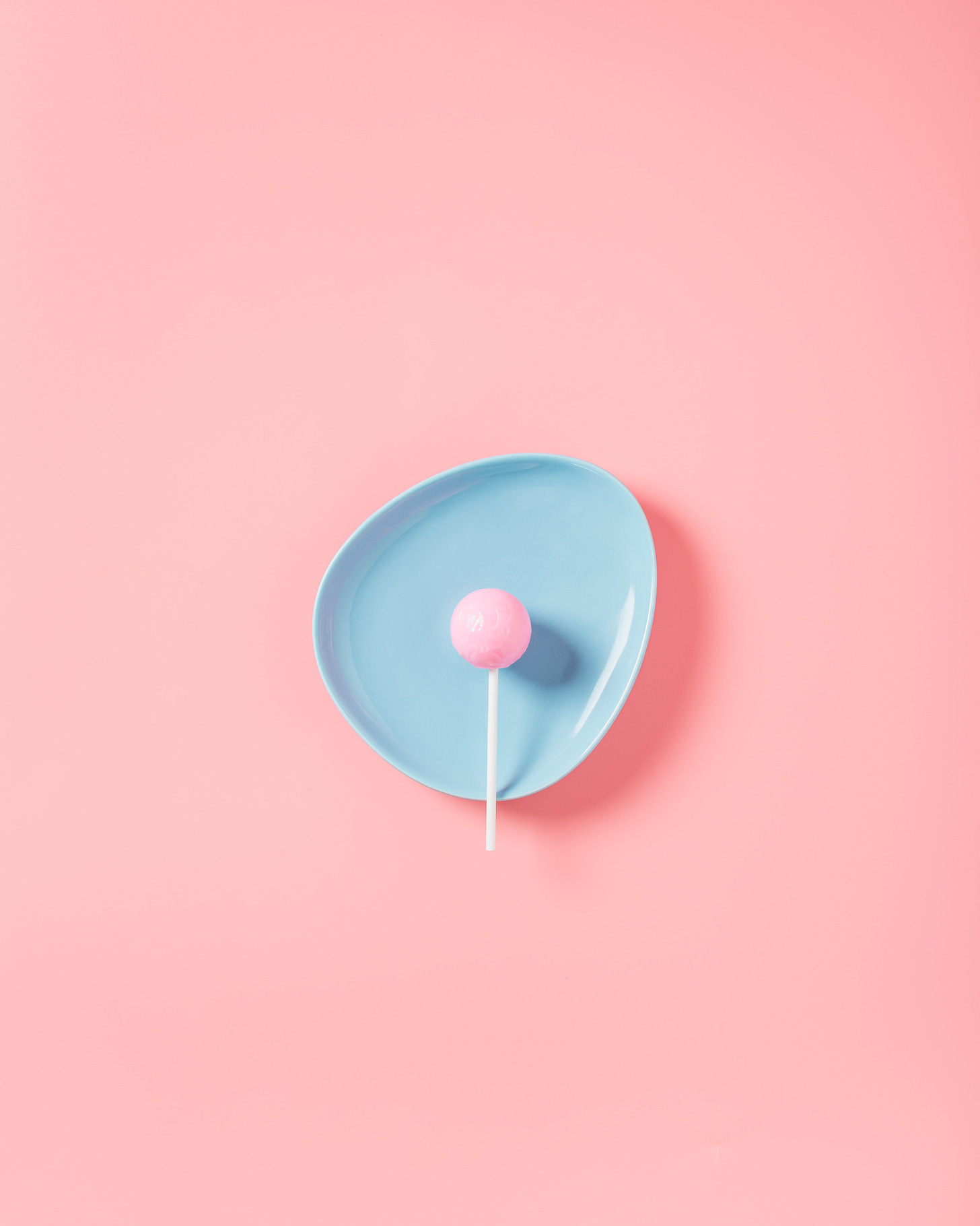 pink sucker on a blue plate against a pink background, very simple