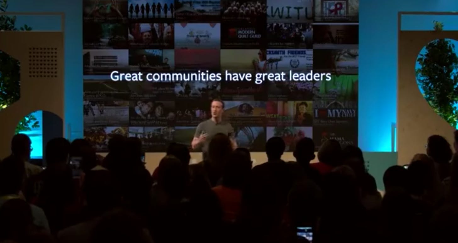 Zuckerberg in front of the crowd that the Communities Summit. It is dark. Zuckerberg is on stage. He stands in front of a presentation that says "Great communities have great leaders." on it