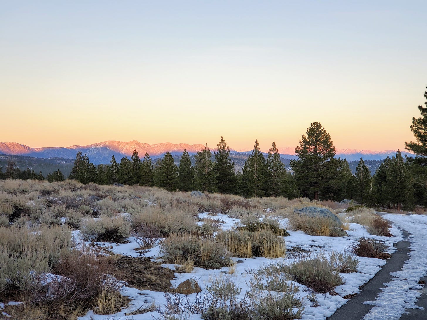 A sunset view of the White Mountains with a snowy trail in the foreground.