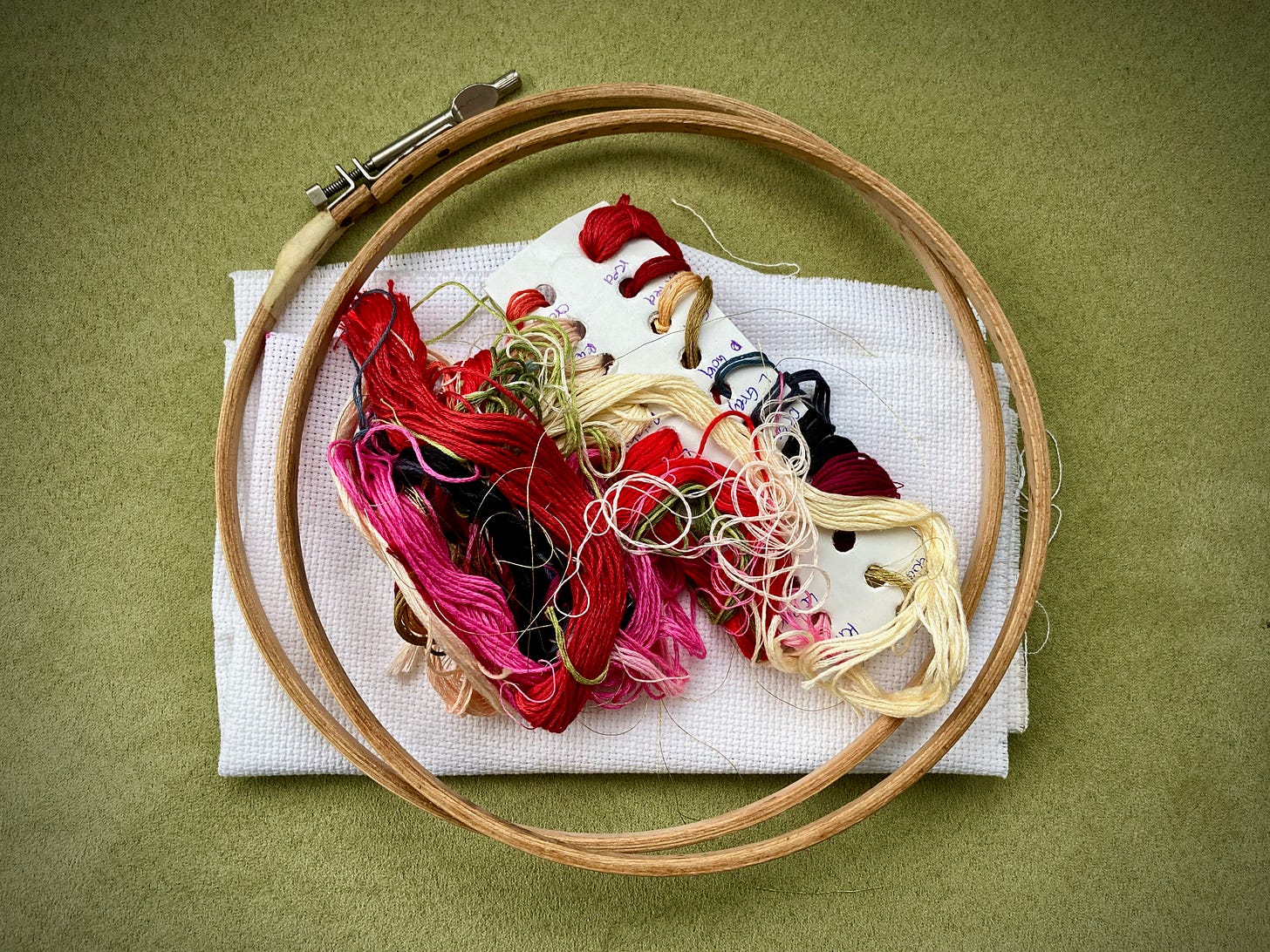 A cross stitch hoop, and the contents of a cross stitch kit: some fabric and threads