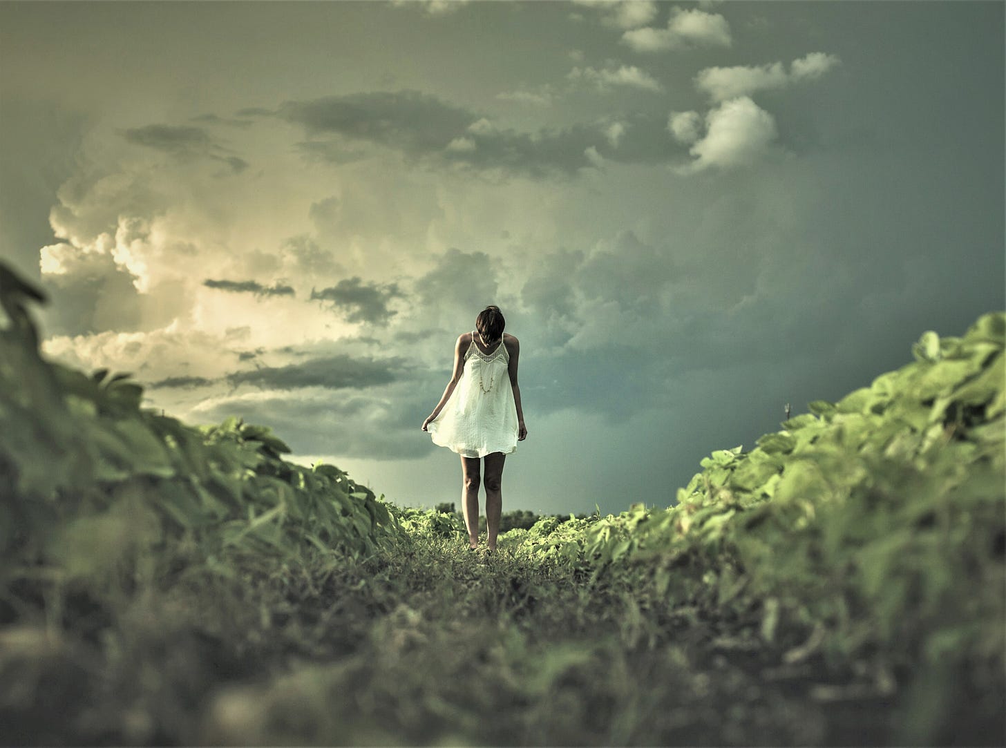 girl in white flowy dress standing in grassy valley with stormy cloudy sky behind her