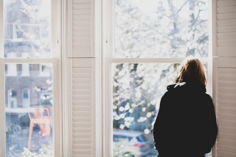 Rearview of a woman looking out a window forlornly.