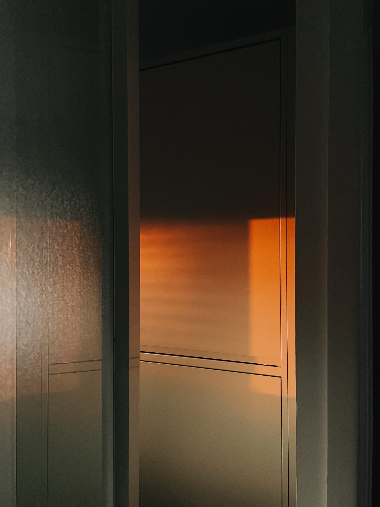 Early morning sunlight on kitchen cupboards seen through a doorway.