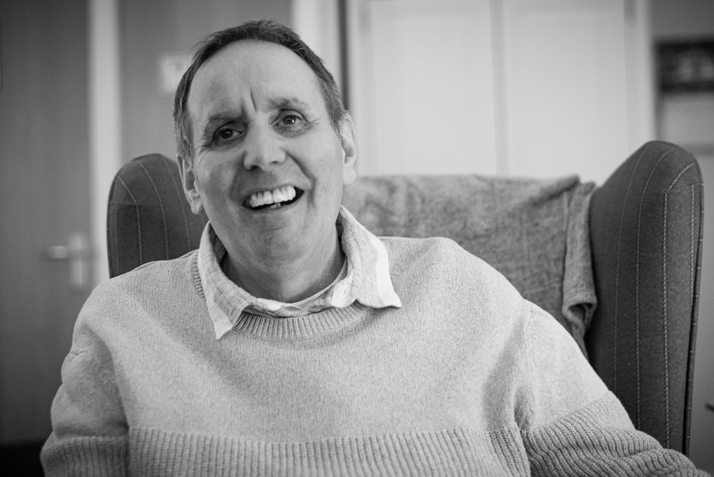 A black-and-white portrait of my dad laughing in his chair.