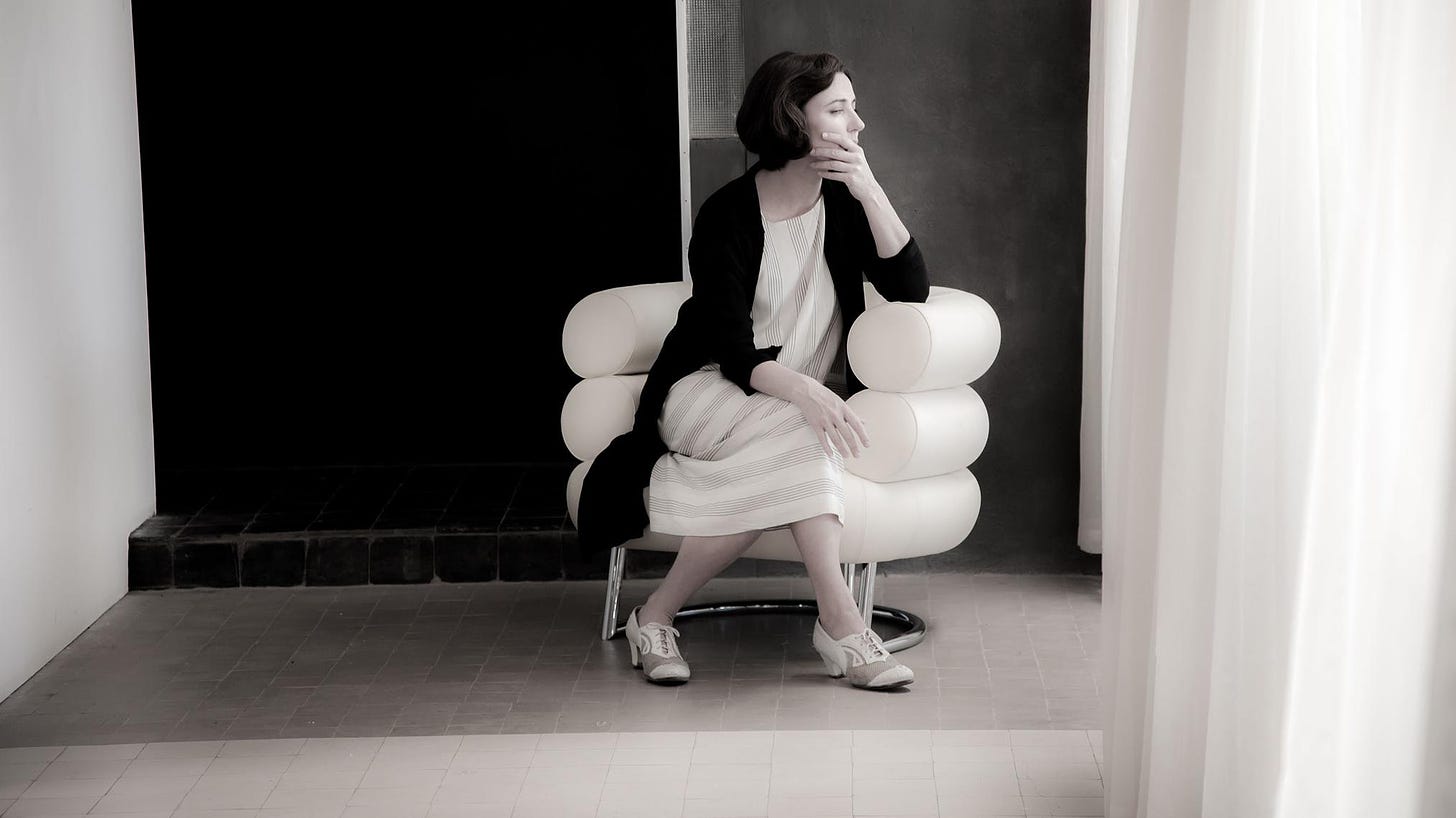 Black and white photo of Eileen Gray sitting in her Bibendum chair, looking into the distance. 