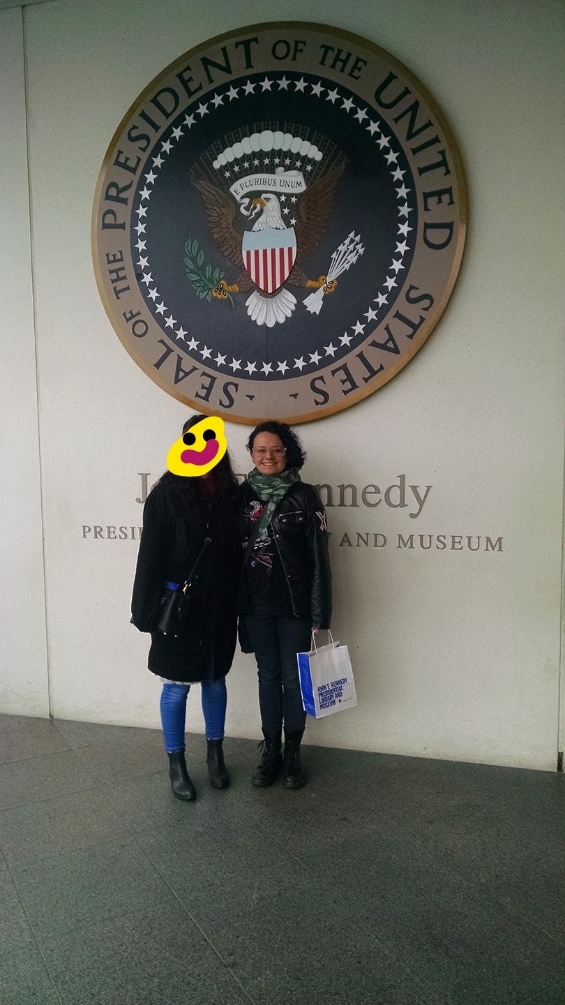 Two white women stand in front of the US presidential seal at the JFK library