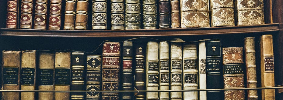 A closeup of many classic elegantly bound books on a wooden bookshelf.