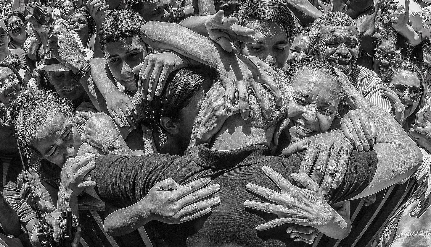 Foto em preto e branco de Lula sendo engolido pelo abraço de uma multidão