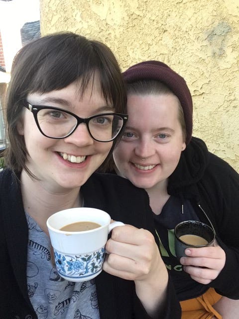 A selfie of Victoria and Healther smiling into the camera while holding mugs of coffee.
