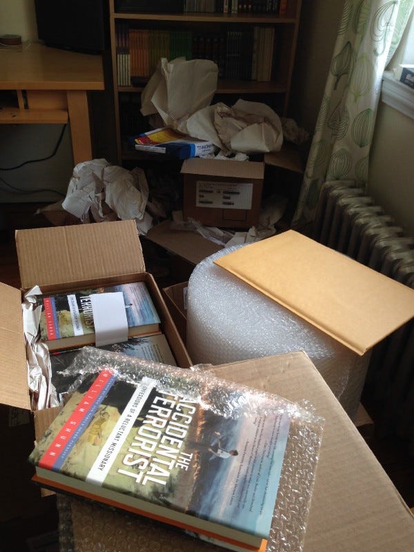 Photograph of the author's home office in 2015, with an open box of copies of his memoir, envelopes and packing supplies, and general clutter.