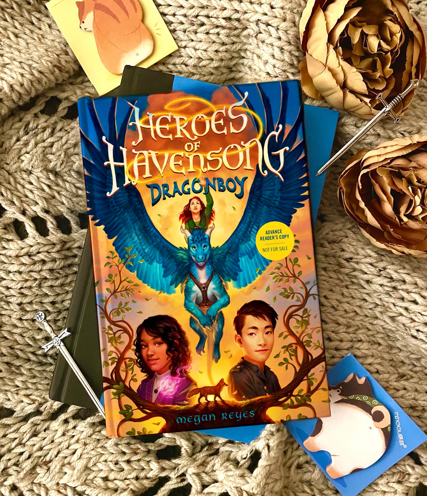 Heroes of Havensong: Dragonboy by Megan Reyes on top of a blue book with a quilted white blanket behind it.