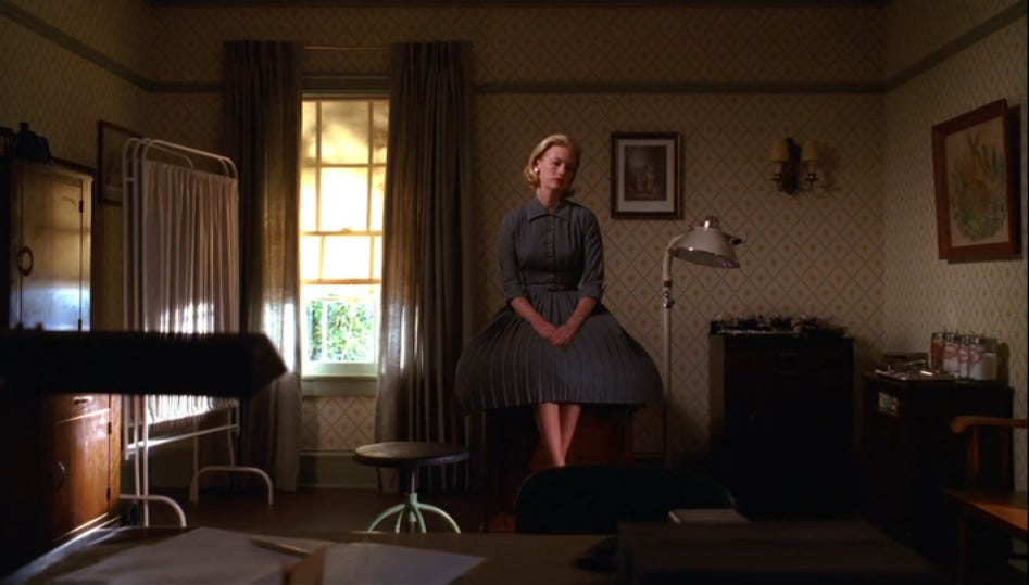 Betty Draper waits in her doctor's office in a gray dress on Mad Men Season 2 Episode 13, Meditations in an Emergency