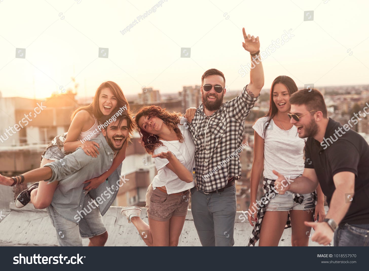 Group of young people having fun at a summertime rooftop party, at sunset. Focus on the people in the middle