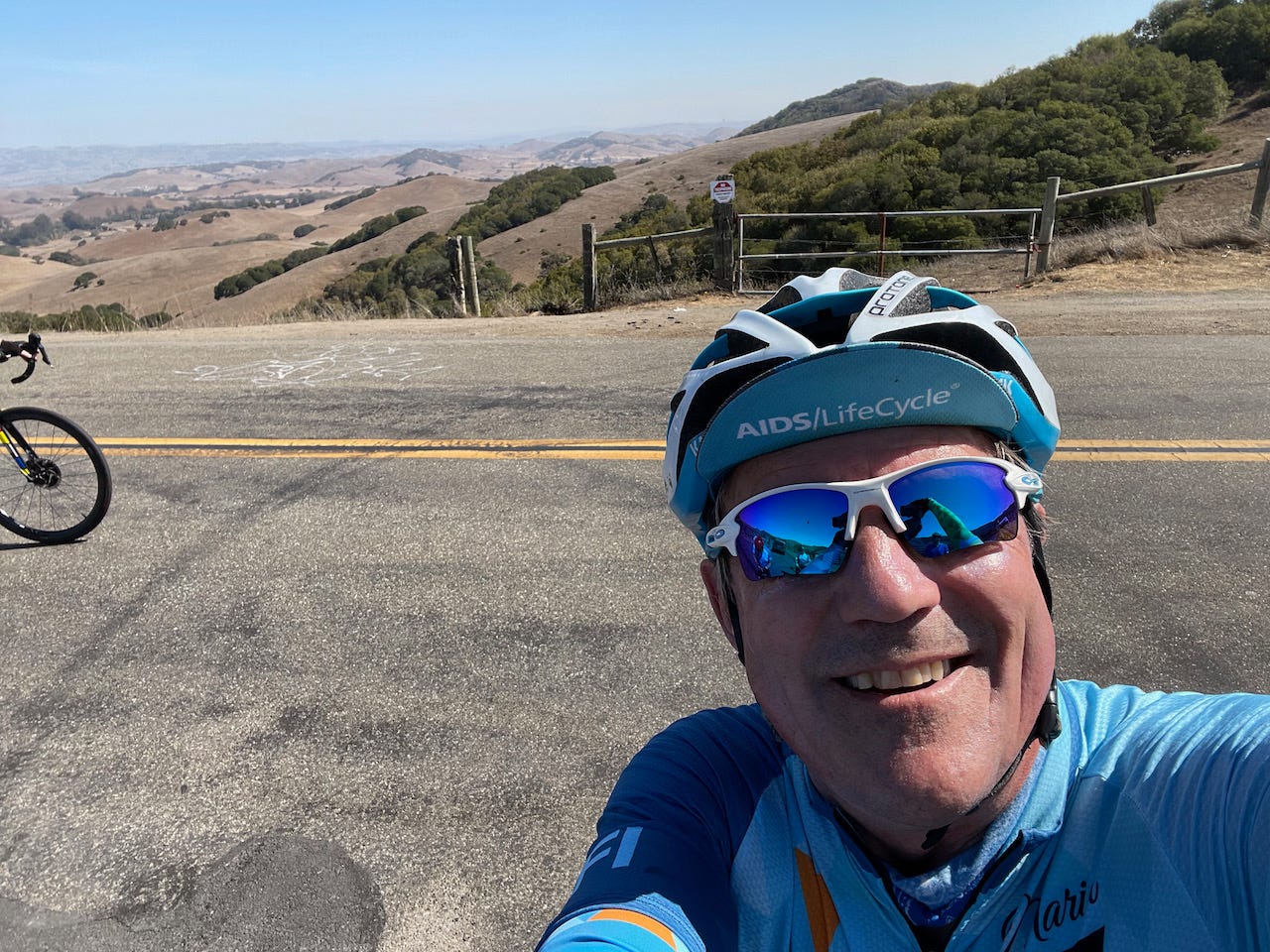 Selfie of the author at the top of the Wilson Hilll climb with panorama in the background.