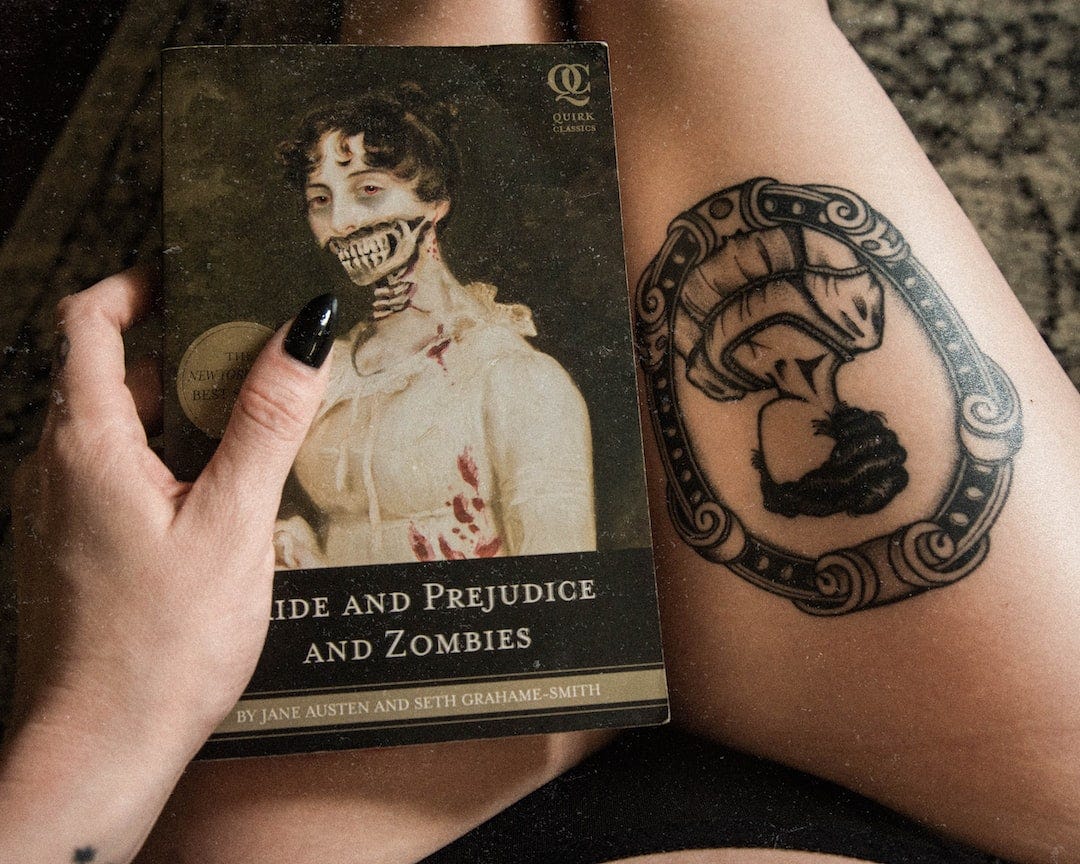 A paperback copy of the book 'Pride and Prejudice and Zombies' rests on the lap of a woman sporting black nails and a black Jane Austen thigh tattoo. 