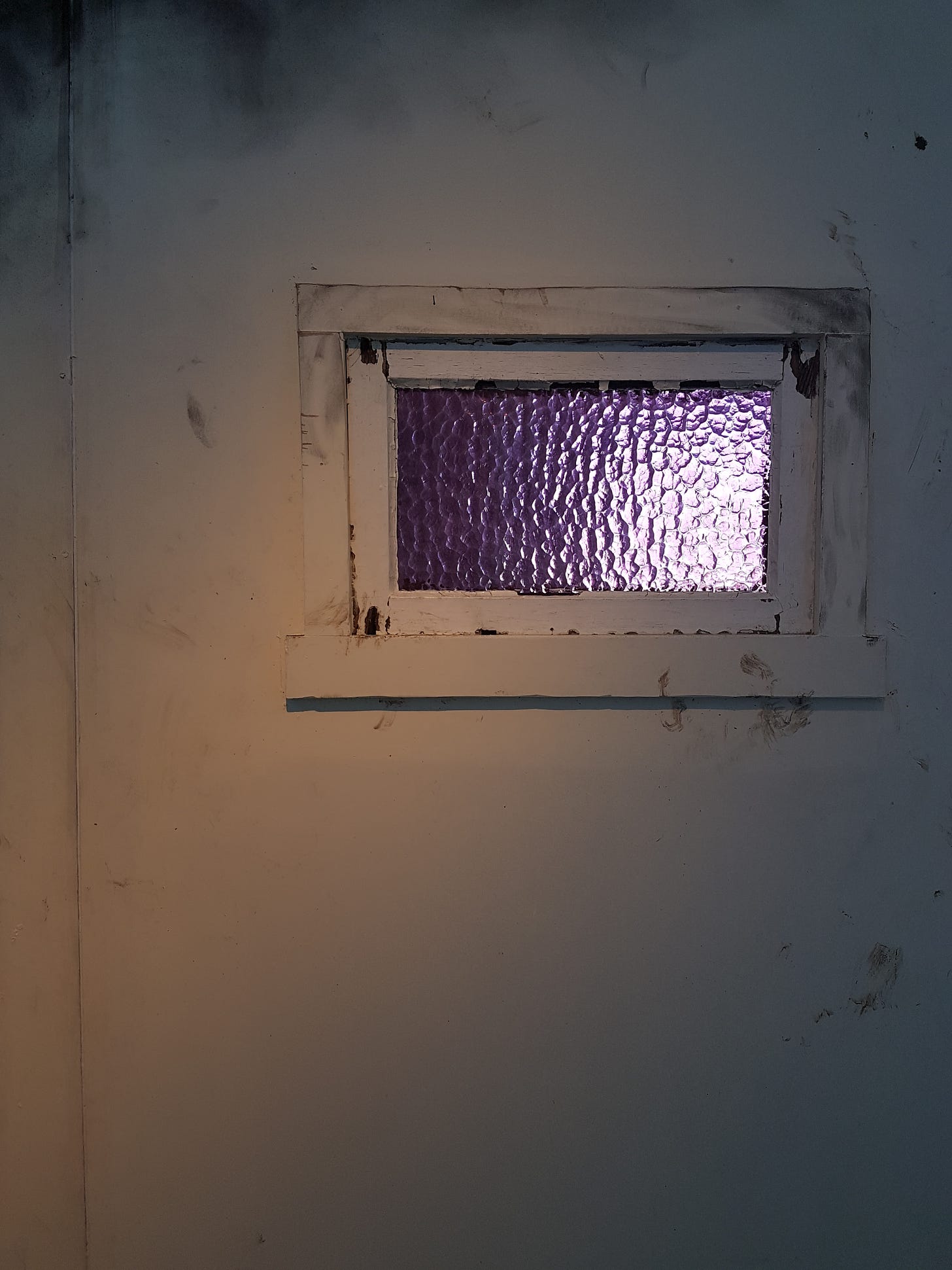 A small purple stained-glass window set within a dirty wall