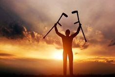 A disabled man raising his crutches at sunset. Positive concept of cure, recovery, medical miracle, hope, insurance etc.