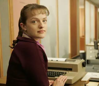The actress Elizabeth Moss as Peggy Olson in Mad Men. She is sitting at an electric typewriter and turning toward the camera