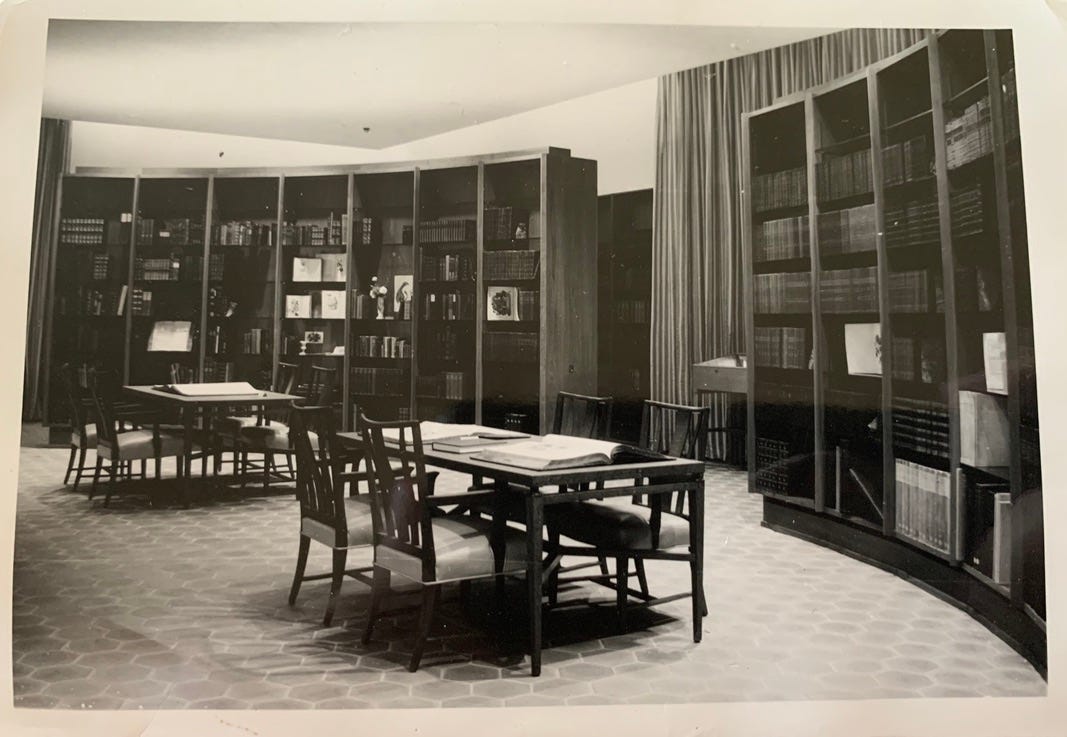 Black and white photo of library tables and oval bookcases.