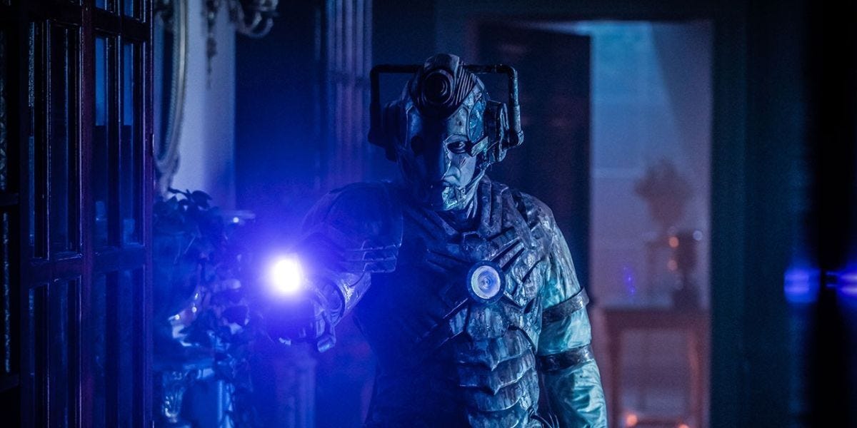 This image shows the Lone Cyberman--Ashad (played by Patrick O'Kane)--standing in a Villa Diodati hallway and pointing the laser blaster on his right arm at camera. Ashad's Cybersuit is rusted and damaged, with a large chunk missing from the left part of his helmet, which exposes Ashad's left eye, left cheek, and the left corner of his mouth. This image shows the Lone Cyberman--Ashad (played by Patrick O'Kane)--standing in a Villa Diodati hallway and pointing the laser blaster on his right arm at camera. Ashad's Cybersuit is rusted and damaged, with a large chunk missing from the left part of his helmet, which exposes Ashad's left eye, left cheek, and the left corner of his mouth.
