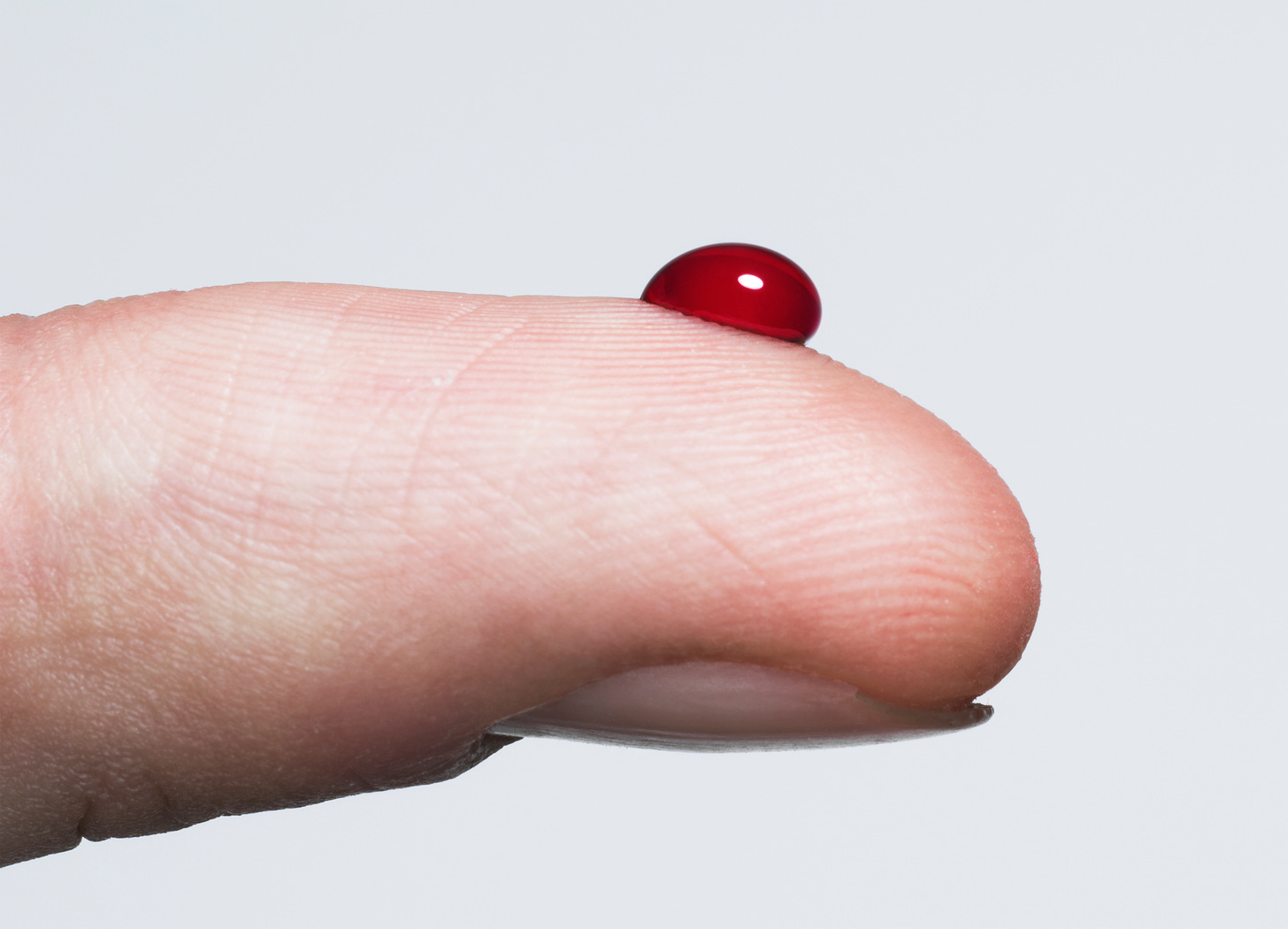 A right index finger close enough that the fingerprints are visible with one single drop of blood the size of a ladybug on it
