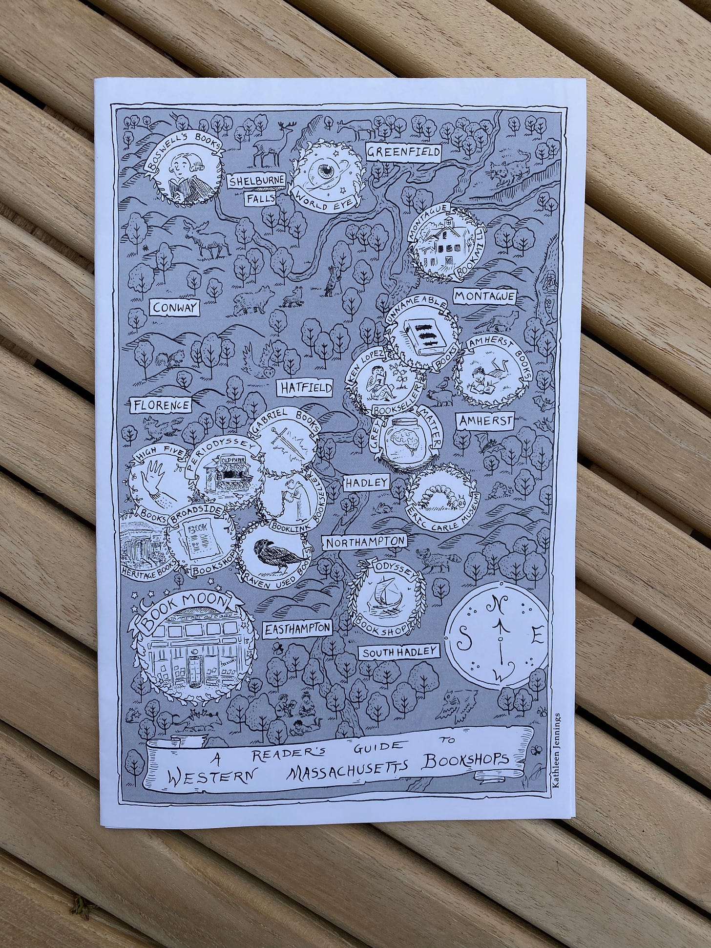 A hand drawn black and white map with stylized illustrations of trees and a river. Small circles with the names of bookstores and their logos appear all over the map, near where the bookstores are actually located. Text at the bottom reads: A Reader’s Guide to Western Massachusetts Bookshops.