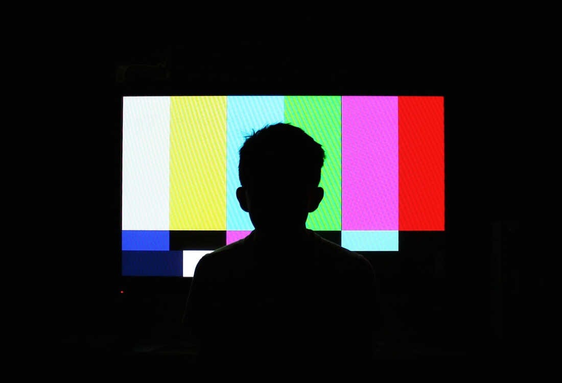 Silhouette of boy in front of a television screen.