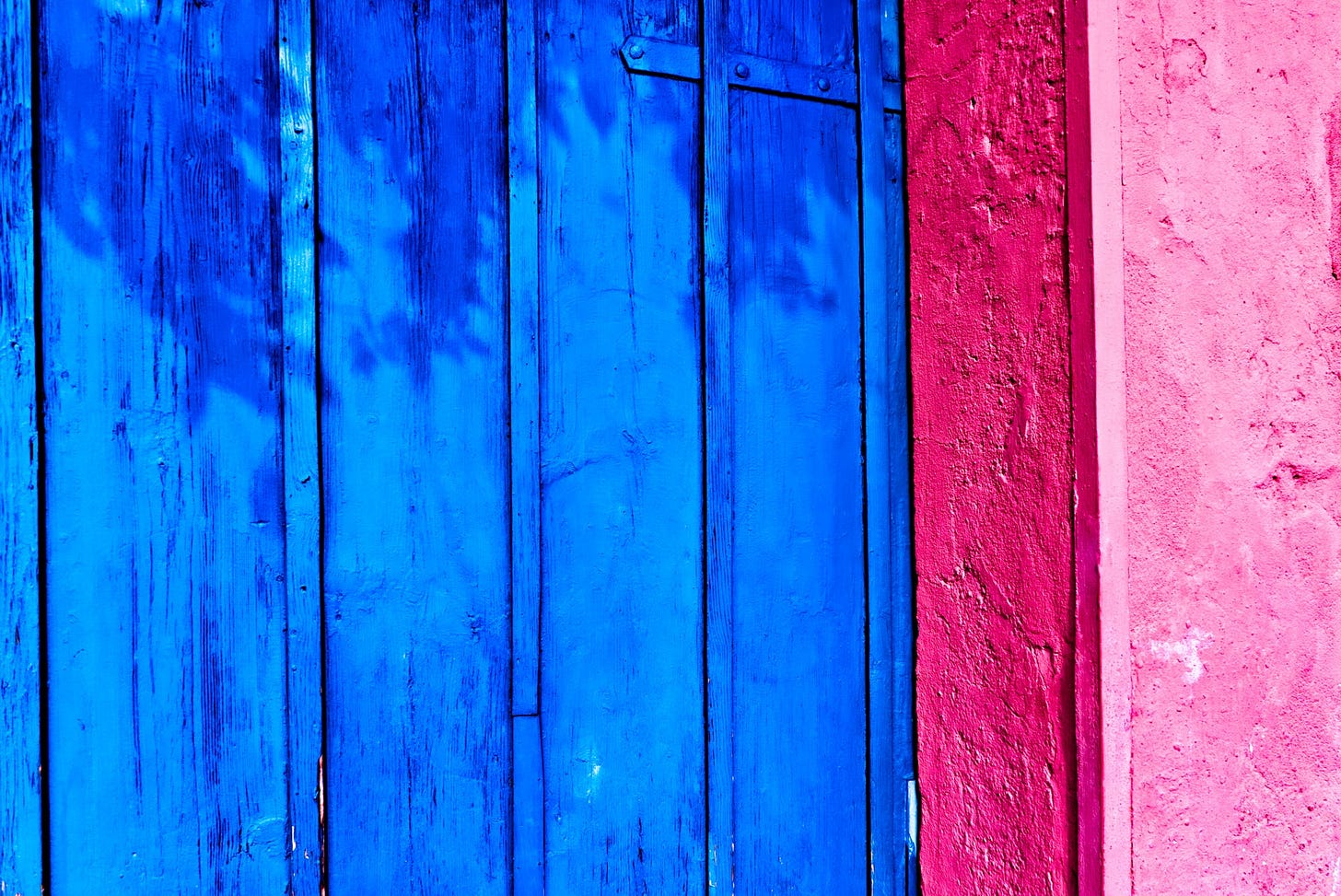 Dettaglio di una porta di legno colorata per metà di blu e per metà di rosa.