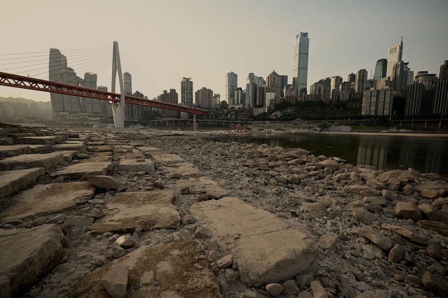 Rocks appear on the dry bed of a river beside a modern city skyline.
