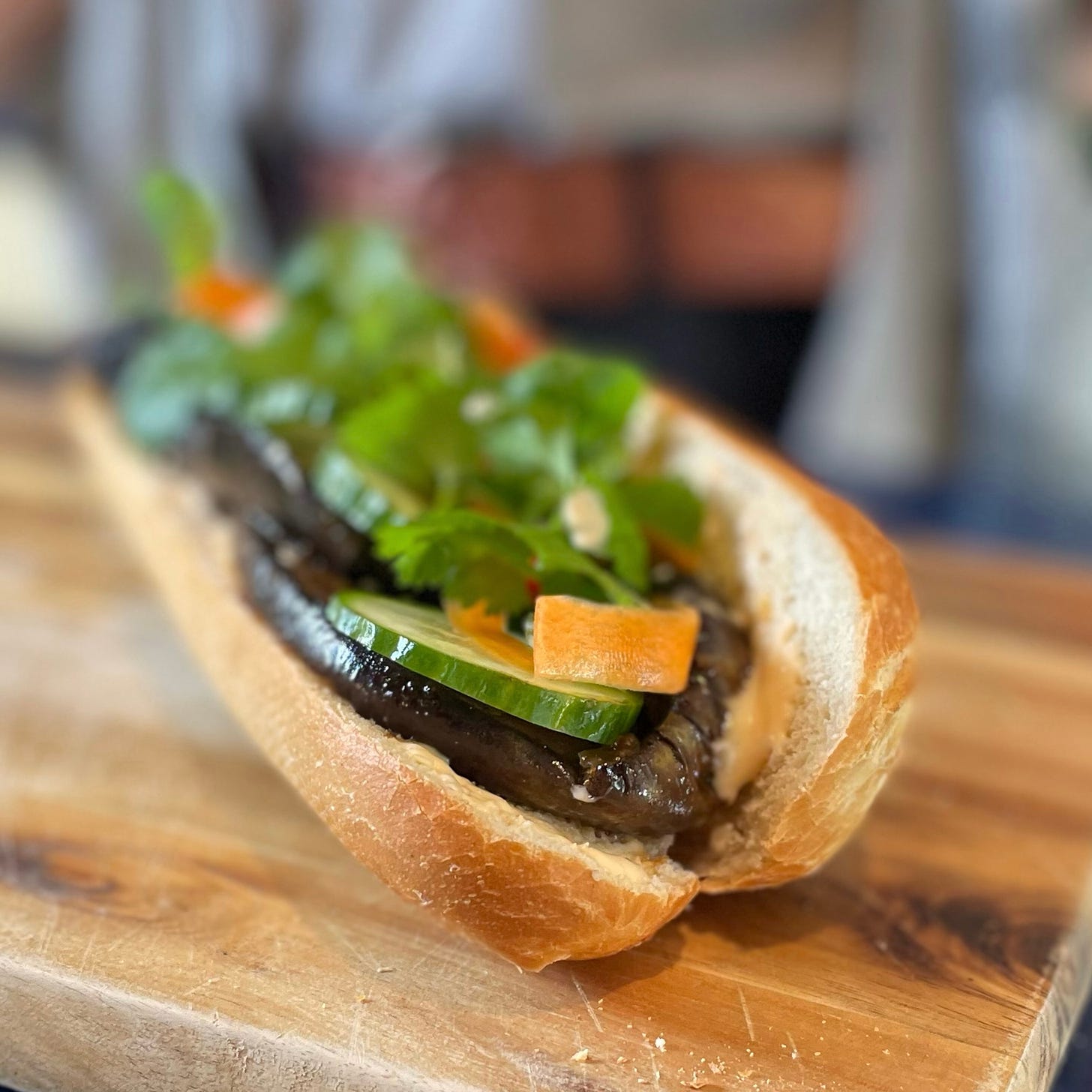 Open baguette filled with sliced aubergine, cucumber, carrot, and herbs
