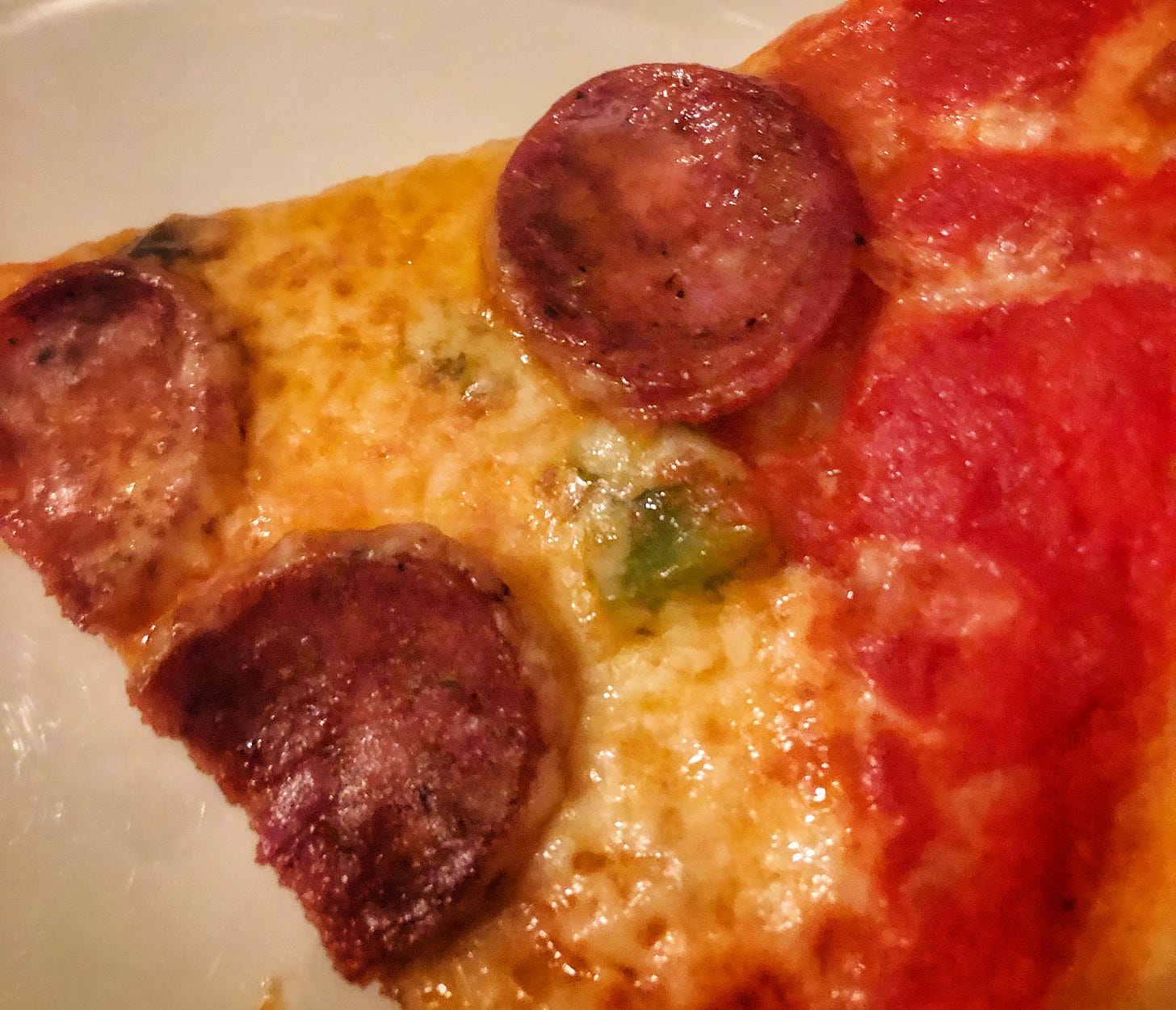 Close up of a slice of pepperoni pizza. The pepperoni has curled up into charred cups.