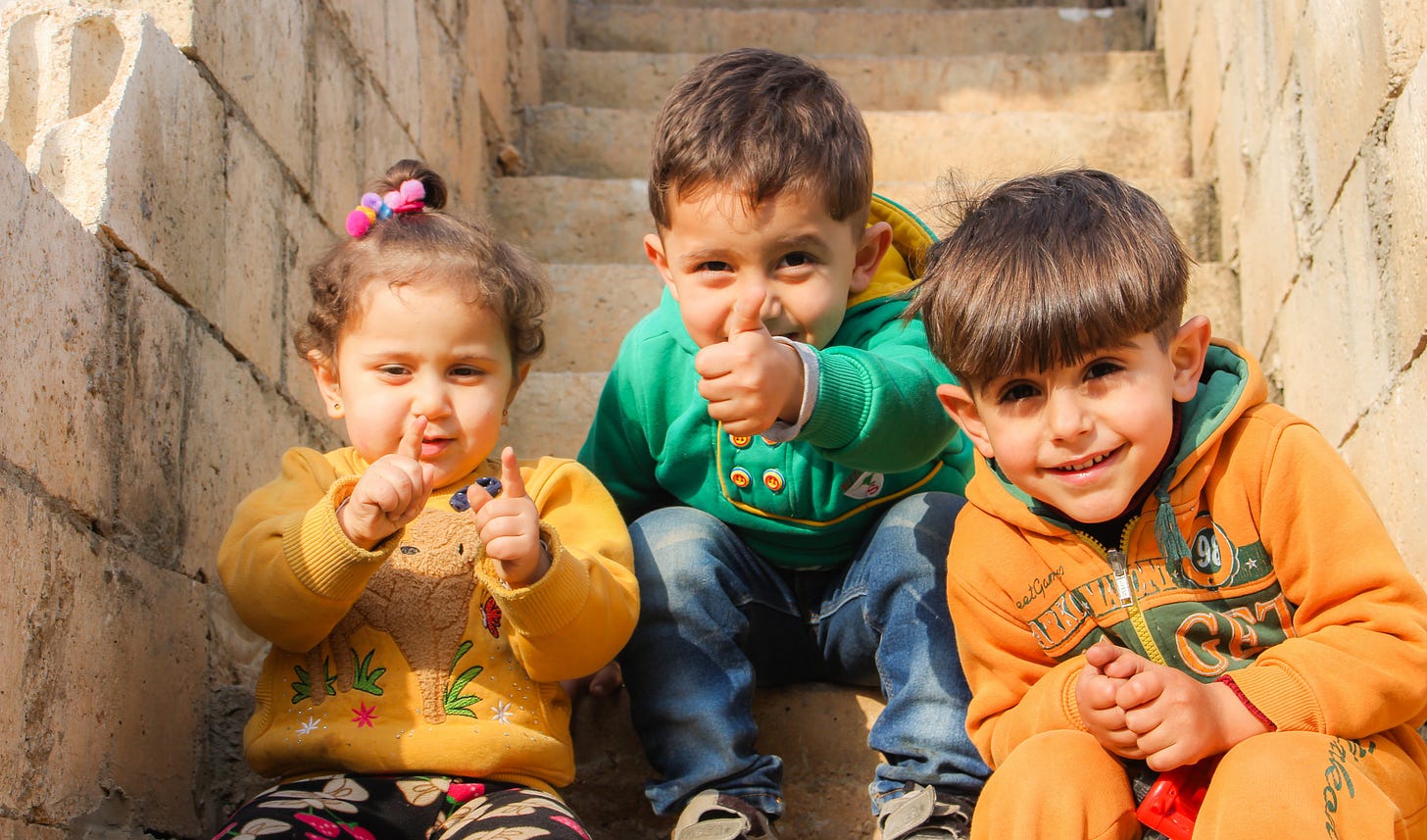 Three small children smiling while sitting on steps.